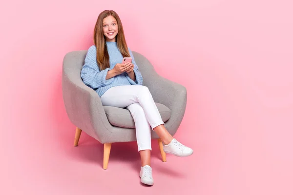 Full length photo of young chilling satisfied teenager schoolgirl chill couch with smartphone browsing information isolated on pink color background.