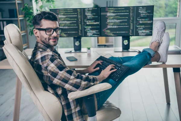 Full body profile portrait of intelligent positive web designer man sit chair put legs table keyboard typing open space indoors.