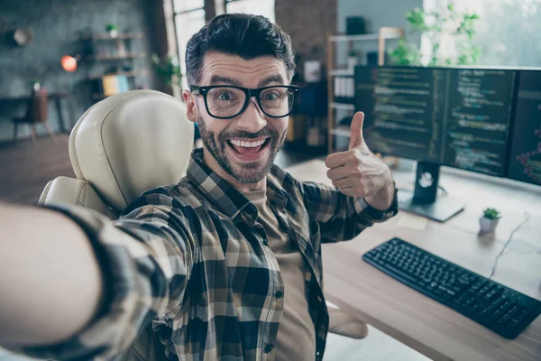 Portrait of excited crazy hacker man sit chair make selfie show thumb up feedback workplace open space indoors.