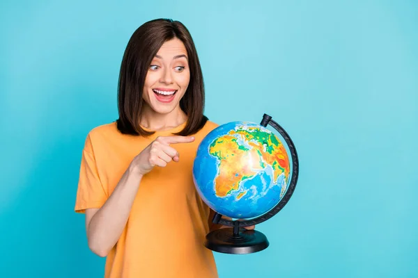 stock image Portrait of positive impressed astonished woman long hairstyle yellow t-shirt look directing at globe isolated on blue color background.