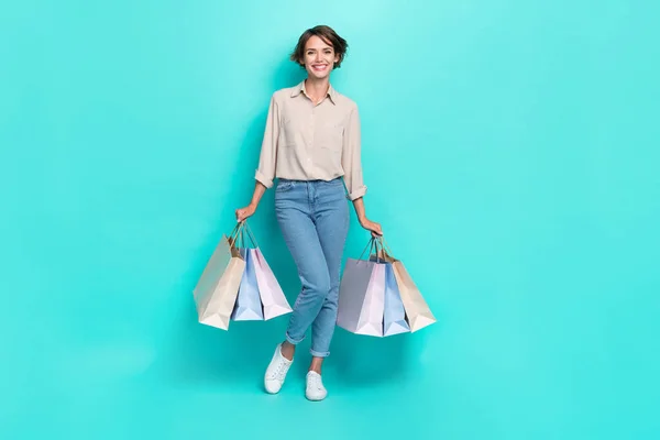 Full length photo of positive pretty lady wear trendy outfit two hand hold carry bags rejoice low price isolated on cyan color background.