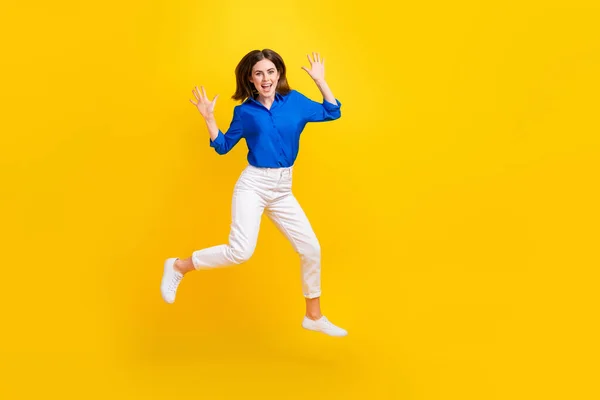 Full length photo of shiny impressed girl dressed blue shirt jumping high empty space isolated yellow color background.