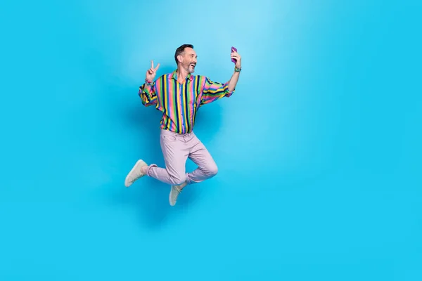Full length photo of positive man feel young recording video photographing hand v-sign empty space isolated on blue color background.