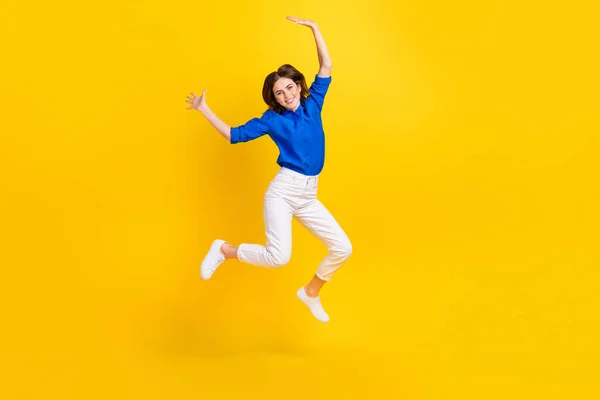 Full length photo of pretty adorable lady wear blue shirt jumping high rising hands arms isolated yellow color background.