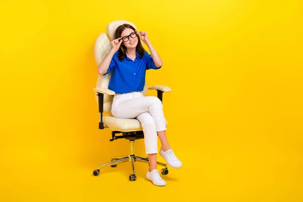 Full body length photo of manager lady wear blue shirt white pants sit chair touch glasses look empty space isolated on yellow color background.