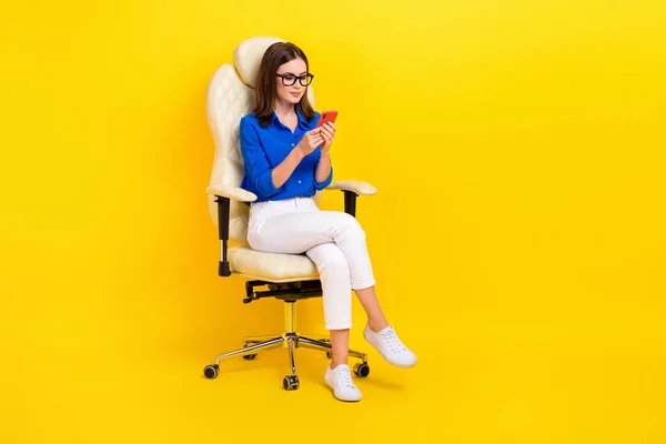 経験豊富なオフィスマネージャー女性のフルボディ写真青いシャツ座ってアームチェア黄色の背景に隔離された仕事のためのスマートフォンガジェットを使用 — ストック写真