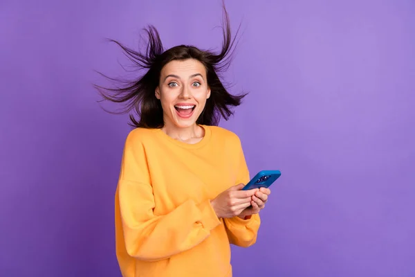 若いクレイジー興奮素敵な女性の写真は 紫の色の背景に隔離されたオンラインプロモーションを予期しない良いオファー携帯電話風の髪を保持スマートフォンを保持します — ストック写真