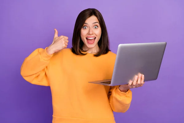 若い愛らしいかわいい素敵な女性の写真は オレンジのシャツを着用紫の色の背景に隔離された記号のような新しいラップトップのFacebookの開発者プログラマーを保持 — ストック写真