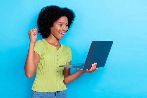 穿着绿色T恤 留着波浪般的头发 喜形于色 喜形于色的女孩的画像 在蓝色背景下被孤立起来的笔记本电脑握紧拳头 — 图库照片