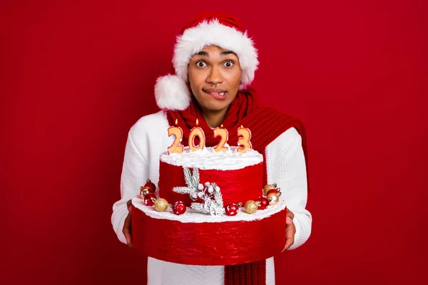 年轻人抱着大圣诞蛋糕咬嘴唇的照片让愿望在红色背景下被隔离 — 图库照片