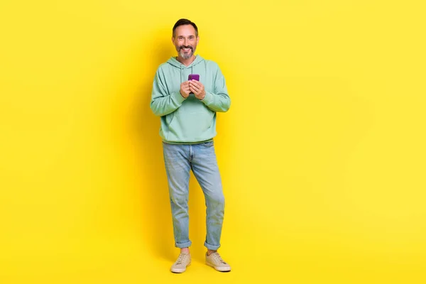 Full length photo of positive satisfied man use quality gadget stand empty space cool offer discount isolated on yellow color background.