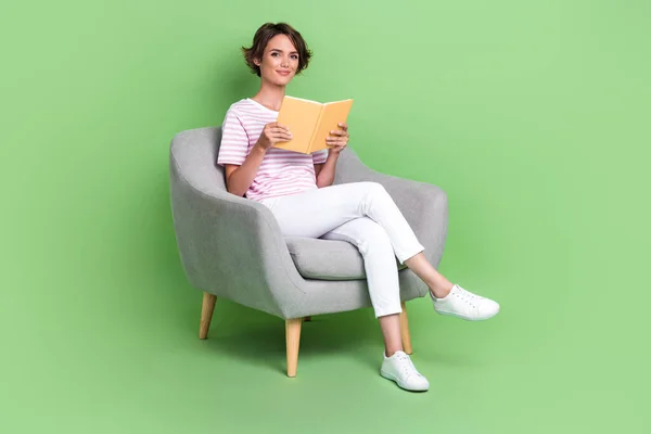 Full body photo of nice young girl soft armchair library enjoy read book wear stylish striped clothes isolated on green color background.