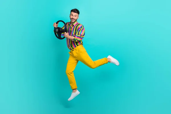 Full length photo of playful handsome man dressed striped shirt yellow pants hold steering wheel isolated on turquoise color background.