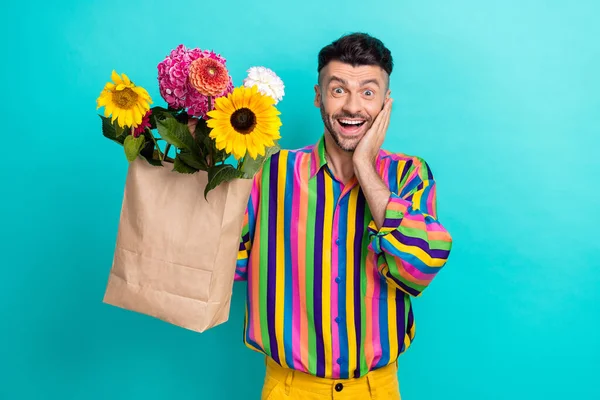 ポジティブな印象的な男の腕のタッチ頬ホールド束の花袋上に隔離されたターコイズ色の背景 — ストック写真