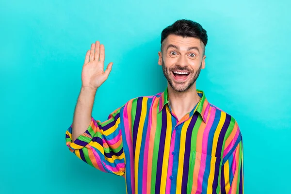 Portrait of good mood handsome guy with brunet haircut wear colorful shirt waving palm say hello isolated on teal color background.