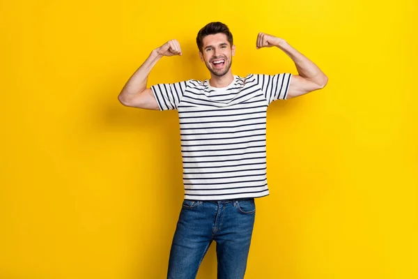 Portrait of satisfied nice young man hands flexing demonstrate biceps isolated on yellow color background.