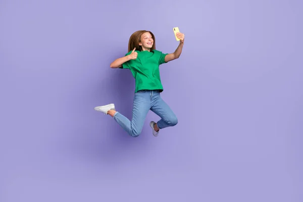 Full length photo of funky cool small lady wear green t-shirt jumping thumb up recording video vlog gadget isolated violet color background.