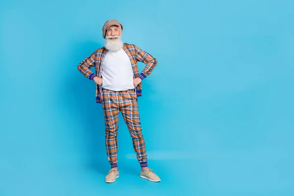 Full length photo of positive funky man dressed trendy plaid clothes hand waist stand empty space isolated on blue color background.