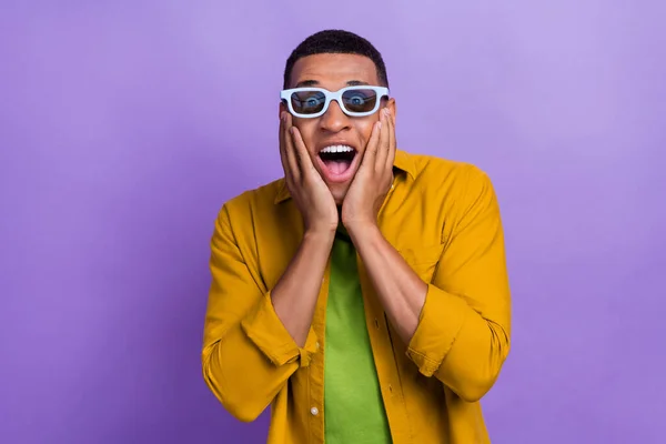 Photo of impressed speechless ecstatic guy dressed yellow shirt 3d glasses palms on cheekbones isolated on violet color background.