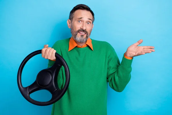 Photo of stressed funny grimace shrug shoulders middle aged man wear green sweater no idea rent service car wheel isolated on blue color background.