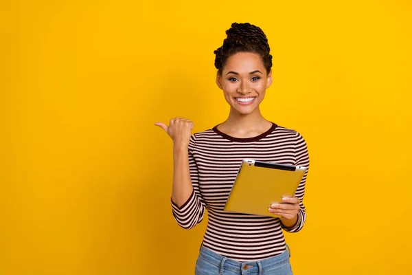 Portrait of attractive positive girl hold tablet indicate thumb finger empty space isolated on yellow color background.