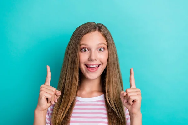 Portrait of astonished charming girl toothy smile direct fingers up empty space isolated on turquoise color background.