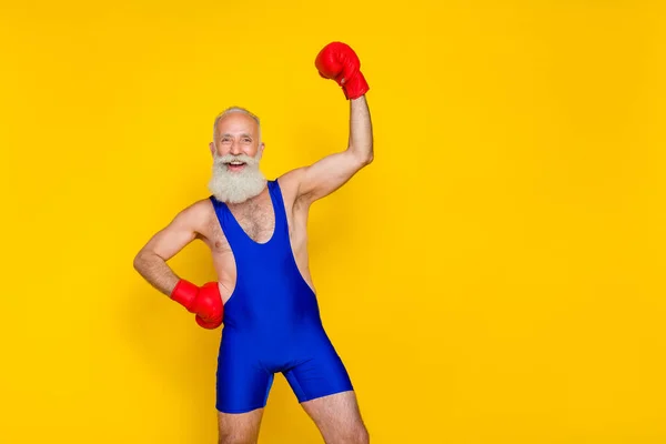 Photo of funny strong man pensioner dressed blue overall red boxing gloves empty space isolated yellow color background.