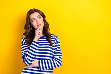 Photo portrait of pretty young girl look skeptical empty space consider dressed stylish striped outfit isolated on yellow color background. clipart