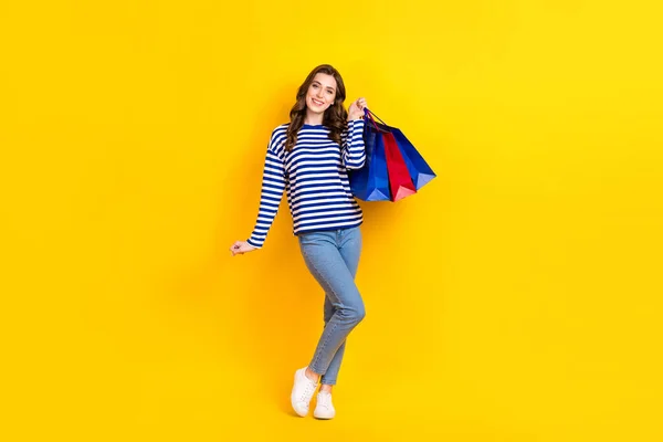 フルボディ写真のかなり若い女の子励起保持ショッピングバッグ服スタイリッシュなストライプ服孤立した黄色の色の背景 — ストック写真