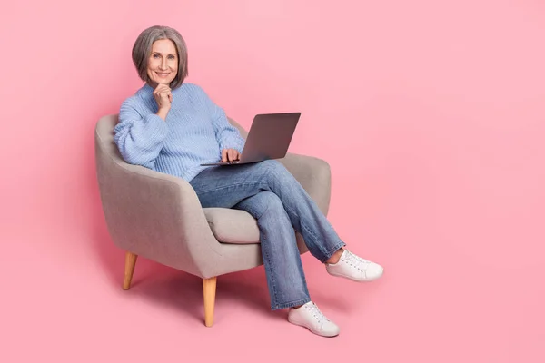 Full body size cadre optimist pensioner woman sit soft chair use laptop modern gadget touch chin for business tasks isolated on pink color background.