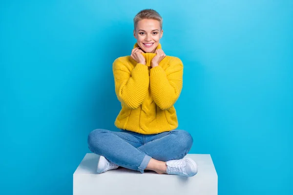 若い正のスタイリッシュな女性の完全な長さボディ写真黄色ニットセータータッチネック快適さ座っている交差脚青の色の背景に孤立 — ストック写真