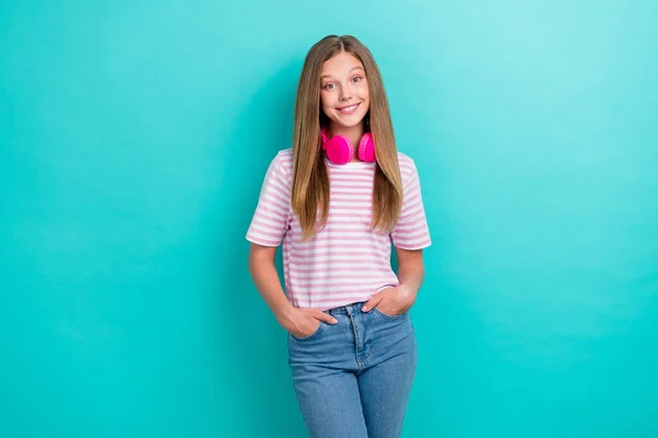 Photo of cheerful adorable girl toothy smile put hands pockets hang neck wireless headphones isolated on turquoise color background.