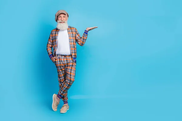 Full length photo of positive man stylish pensioner gentleman wear vintage suit arm present empty space isolated on blue color background.