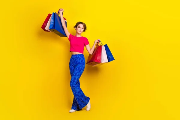 Full length photo of lovely glad lady wear pink clothes hold packs rejoice nice shopping empty space isolated on yellow color background.