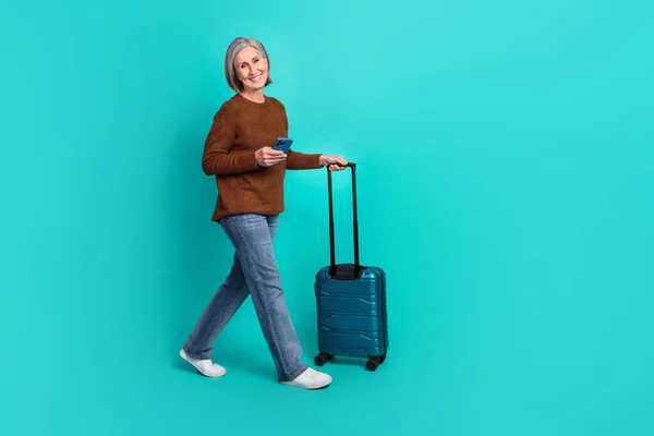 Full body profile photo of nice positive lady hold telephone suitcase walking empty space isolated on turquoise color background.
