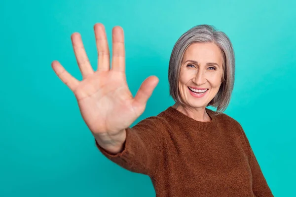 Photo of cheerful lady pensioner wear brown stylish clothes waving hand hi good mood isolated on cyan color background.