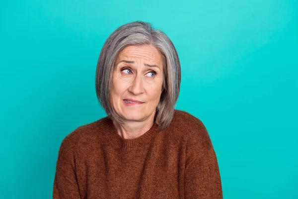 Photo of nervous aged person biting lips look interested empty space isolated on aquamarine color background.