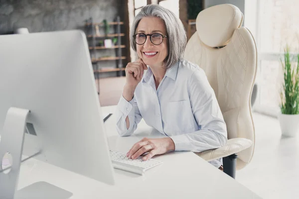 魅力的な素敵なシニア年金受給者の女性の写真 明るい現代的な作業ステーションがコンピュータを入力座って陽気な笑顔オンライン会議 — ストック写真