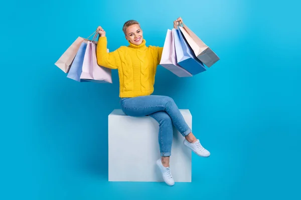 Full length photo of charming blonde short hairdo woman hold stack packages from black friday sit platform isolated on blue color background.