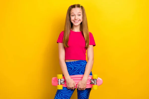 Portrait of cute good mood satisfied active girl with long hairdo dressed pink top hold skate board isolated on yellow color background.