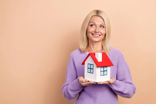 Photo of minded positive person hold little house look empty space isolated on beige color background.