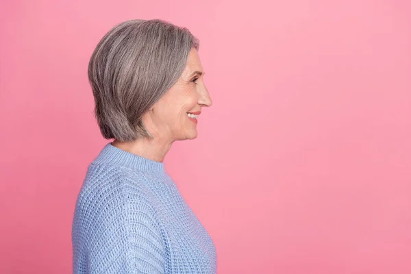 Side profile photo of mature aged old senior cheerful grandmother woman gray hair smiling looking empty space ad isolated on pink color background.