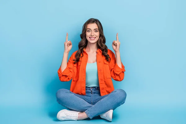 Full body photo of young lovely lady sitting floor point up empty space dressed stylish orange clothes isolated on blue color background.