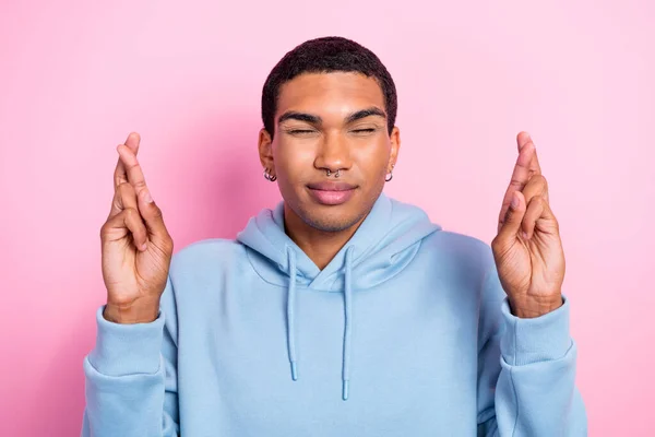 面白い祈りの若い男の肖像青のスポーツウェアのスウェットシャツを保持指を交差近い目の欲望ピンクの色の背景に孤立 — ストック写真
