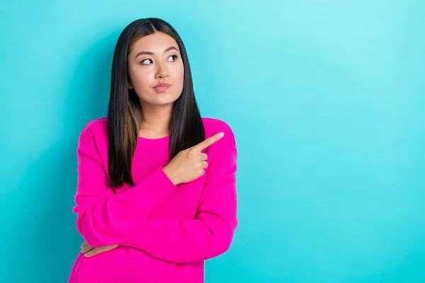 Photo of minded japanese pretty woman wear pink knitted pullover indicate finger empty space pouted lips minded isolated on blue color background.