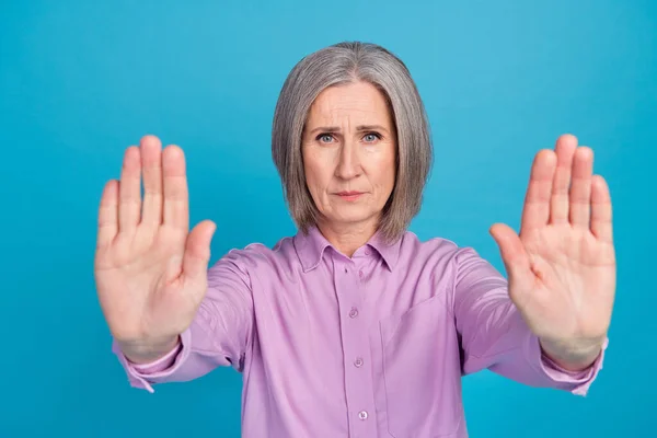 Photo of serious lady pensioner wear violet stylish clothes demonstrate two arm palm dont come isolated on blue color background.