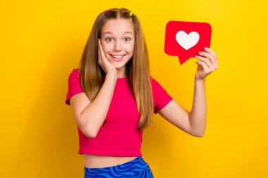 Photo of young teen age girl wearing pink t-shirt touch cheekbones hold notification like symbol enjoy blogging isolated on yellow color background. clipart