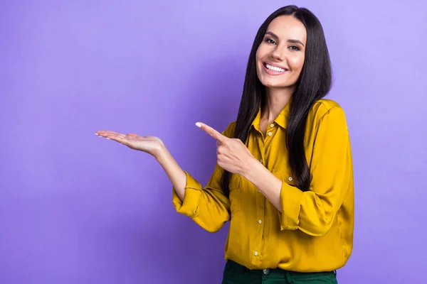 Photo of gorgeous cheerful girl beaming smile direct finger arm hold empty space isolated on violet color background.