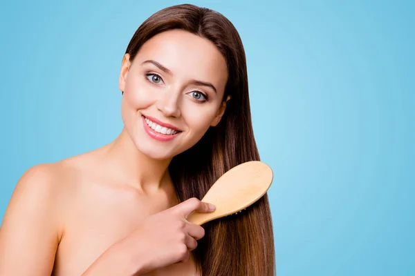 Concept of healthy good hair. Pretty beautiful charming woman with beaming smile is brushing her long brown straight shiny hair, isolated on grey background.