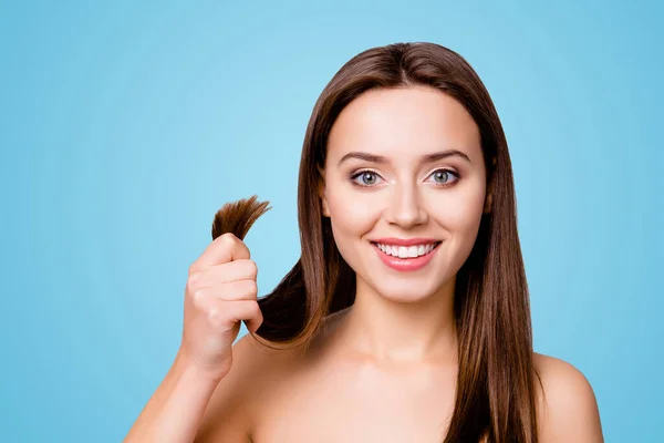 Concept of finding a good solution in treating damaged hair ends. Pretty cute smiling woman is showing her healthy hair, isolated on grey background.